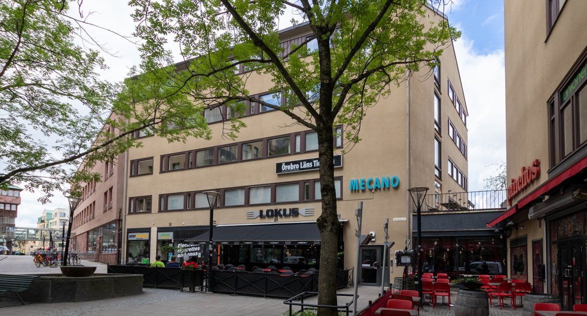 Fastighet på Näbbtorget i Örebro, beiget hus i flera våningar med restaurang och uteservering i bottenplan.