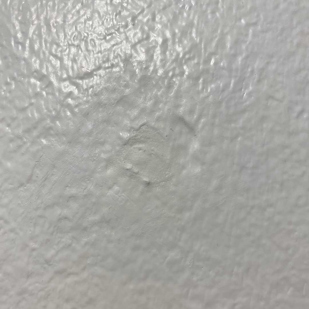 Närbild på godkänt spacklat hål som matchar väggen och utan spackelmassa utanför hålet.